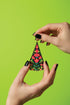 A pair of hands holding a colorful, beaded earring against a bright green background.